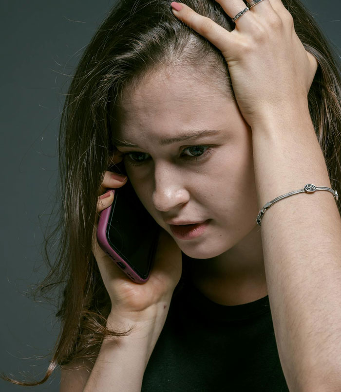 Young woman looking distressed while talking on phone, reflecting on cutting off friend in abusive marriage situation.