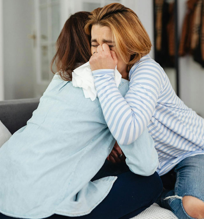 Two women comforting each other, one crying and holding tissues, reflecting on staying in an abusive marriage and friendship struggles.