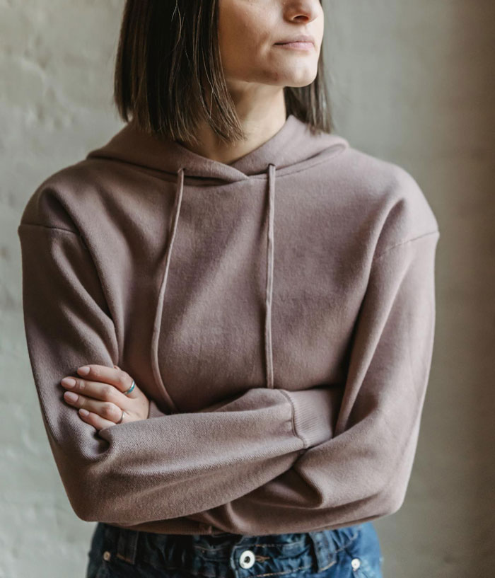 Young woman in a hoodie with crossed arms, reflecting on friendship and staying in an abusive marriage situation.