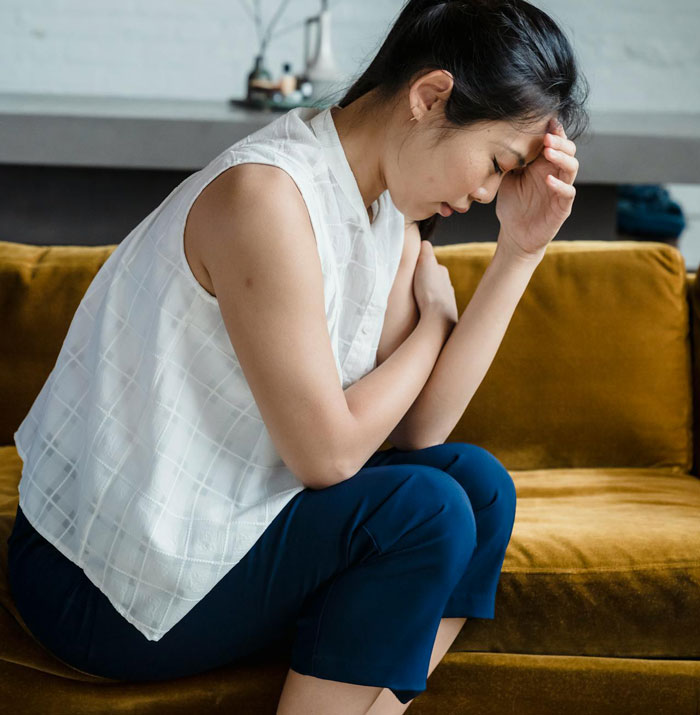 Woman sitting on a couch looking distressed, reflecting feelings related to cutting off a friend in an abusive marriage