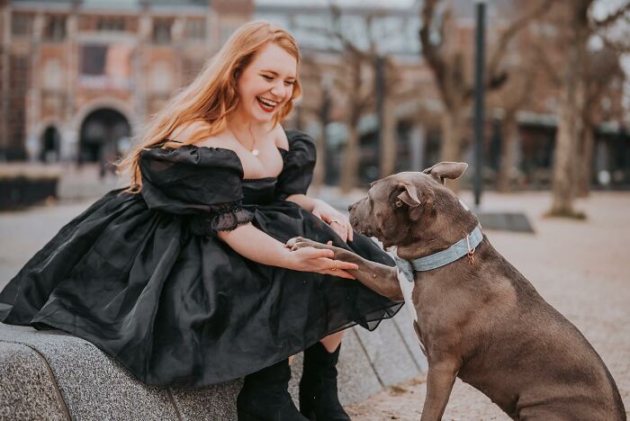Young woman in a black dress smiling and holding paws with a dog, symbolizing people talk about women facelifts harm. - 2