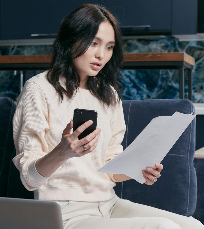Woman reviewing documents and holding phone with a surprised expression related to prenup and insurance discussion.