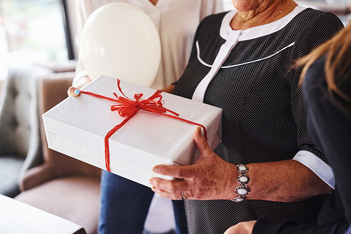 Woman receiving a gift wrapped in white paper with red ribbon, illustrating jerk boyfriend buying dream gift for someone else. - 10