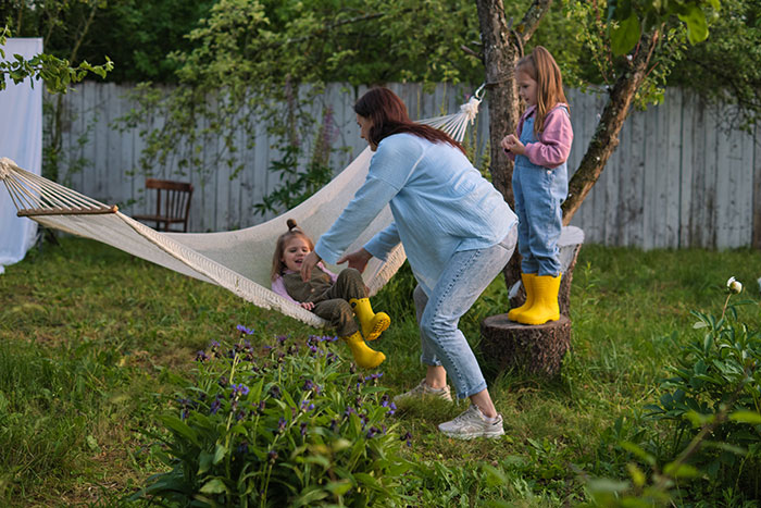 Woman babysitting children in backyard, playing with them near a hammock on a sunny day. - 1