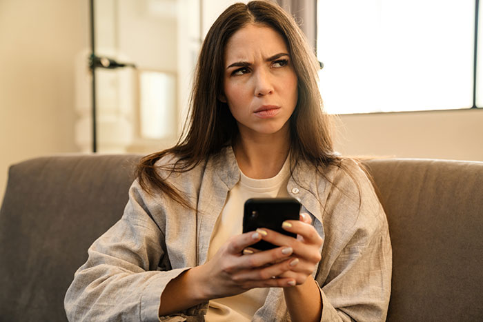 Woman sitting on couch looking upset while holding phone, reflecting frustration after being used as babysitter. - 5
