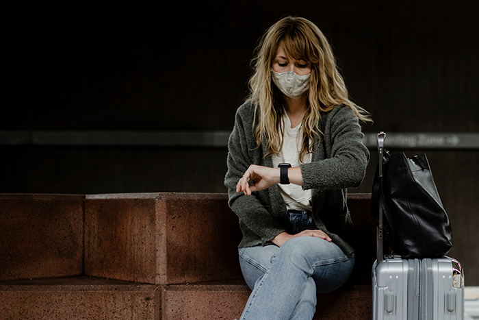 Woman wearing mask sitting with suitcase, looking at watch, reflecting on organ donor refusal and apology request. - 1