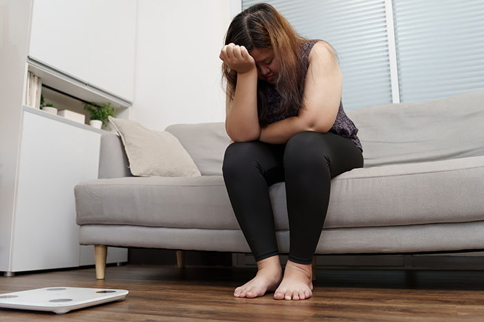 Woman sitting on a couch looking shocked and upset after overhearing boyfriend&rsquo;s parents talking about her.