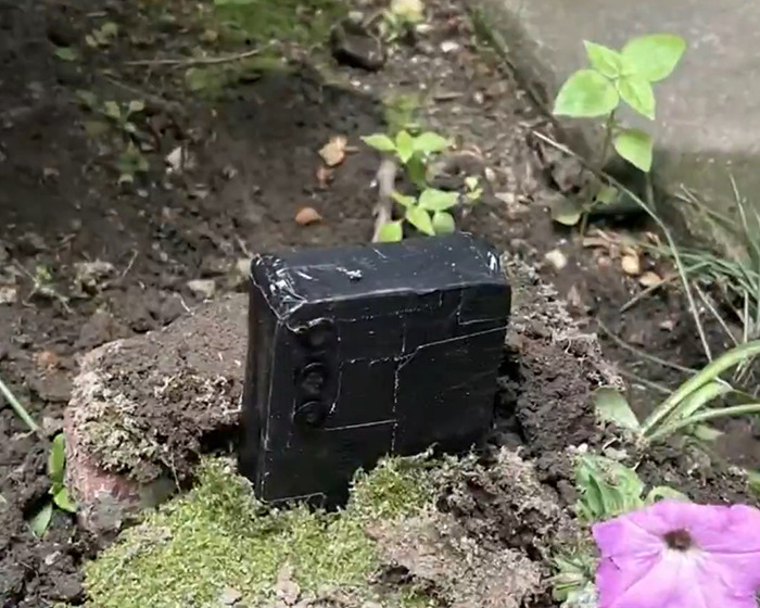 Black phone partially buried in soil in a garden setting, highlighting a woman discovers phone trend warning by police. Black phone partially buried in soil in a garden setting, highlighting a woman discovers phone trend warning by police.