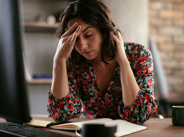 Woman looking stressed at desk, wearing a floral dress, contemplating refusing to wear niece&rsquo;s handmade dress for career event.