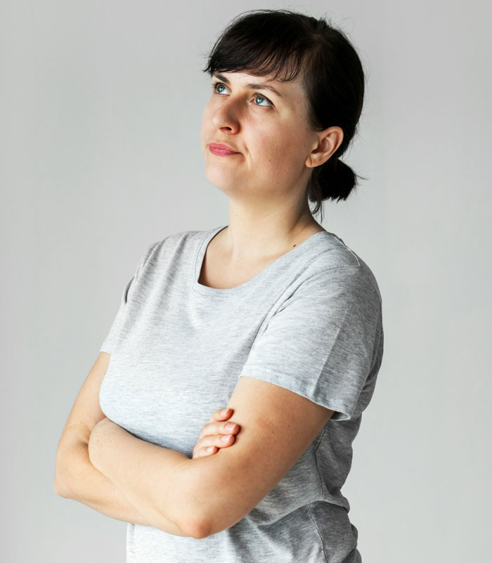 Woman refusing to wear niece&rsquo;s handmade dress, arms crossed, looking away thoughtfully in a plain gray shirt.