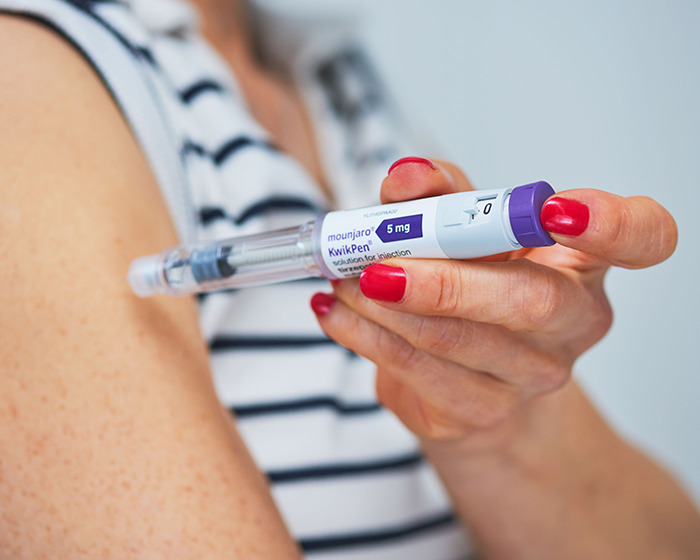 Close-up of woman holding Mounjaro injection pen with red nail polish, preparing for self-administration in arm. - 3