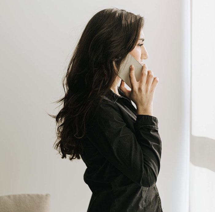 Woman with long dark hair in black shirt making a phone call, reflecting the topic of partner becoming homeless after her death.
