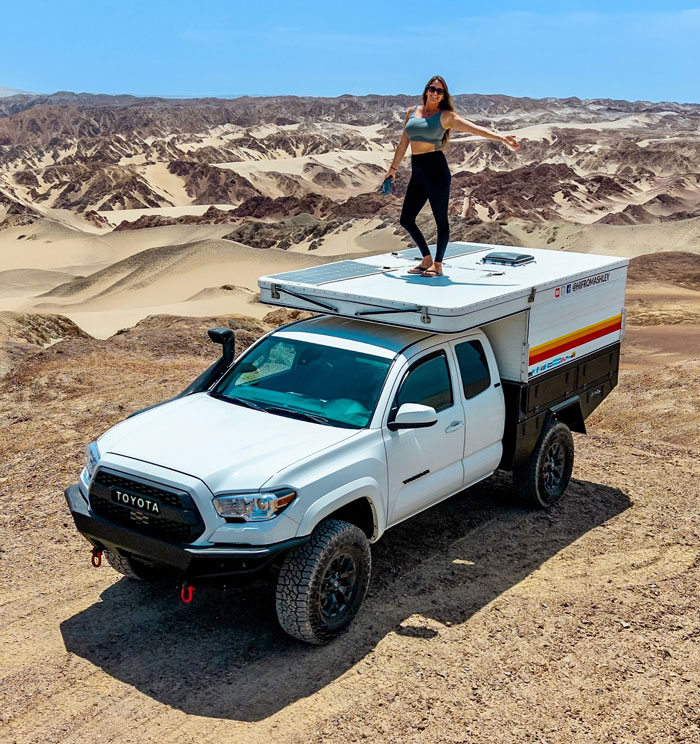 Woman standing on roof of white van in desert landscape, embracing van travel and adventure lifestyle. - 1
