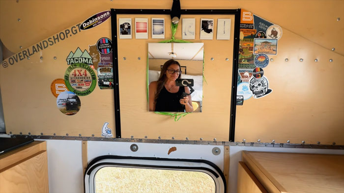 Woman traveling the world in her van takes a selfie in a decorated camper interior with travel and adventure stickers. - 4