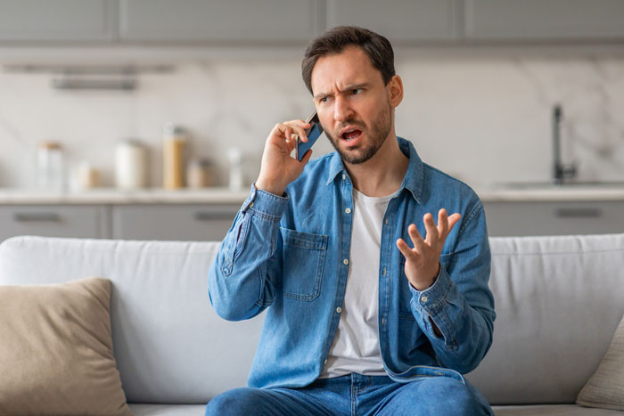 Man in casual denim shirt looking frustrated while talking on phone at home, reflecting supervisor&rsquo;s order issues.