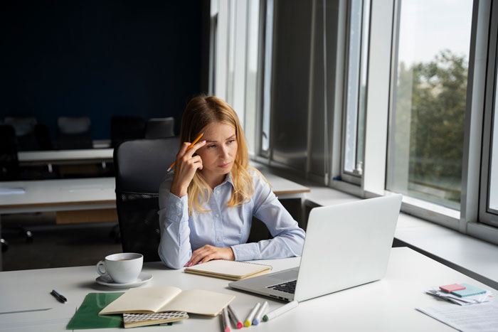 Woman at office desk looking unmotivated while working on laptop, illustrating lazy worker doing the bare minimum.
