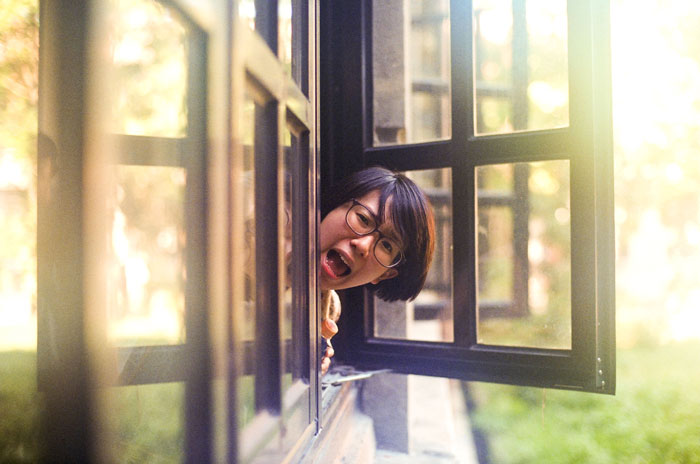 Woman looking surprised and frustrated while leaning out of a window, illustrating coworker demands and ride requests.