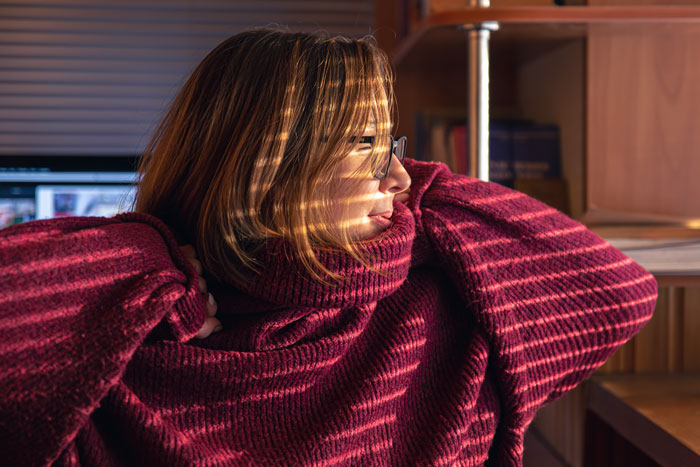 Woman in a red sweater looks contemplative indoors, relating to coworker moving in and demanding rides without notice.