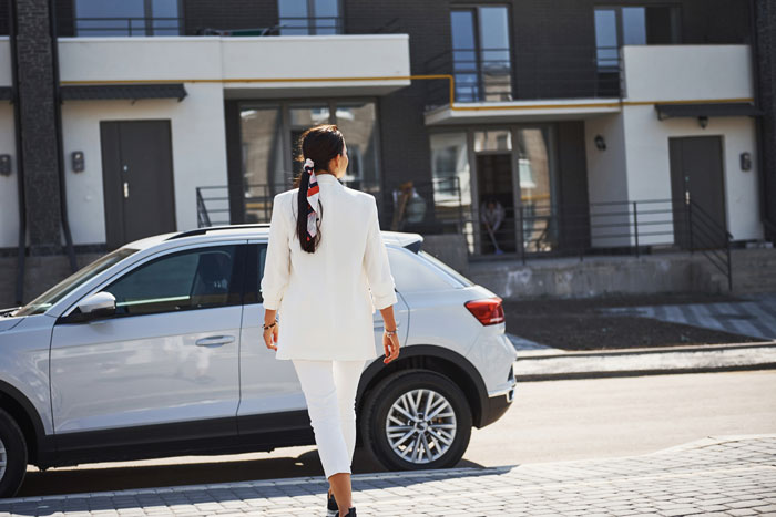 Woman in white walking toward her car outside a modern building, illustrating coworker demanding rides with no notice or tact.