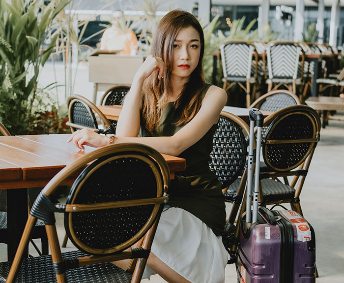 Young woman sitting alone at a restaurant table with a suitcase, representing servers sharing the worst dates witnessed at work.