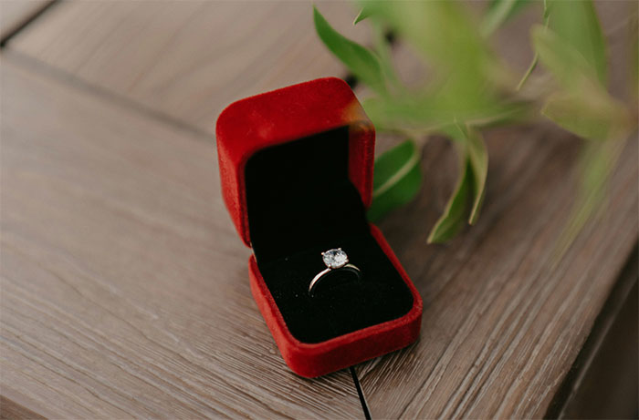 Engagement ring in a red velvet box on a wooden table, symbolizing worst dates servers had to witness at work.