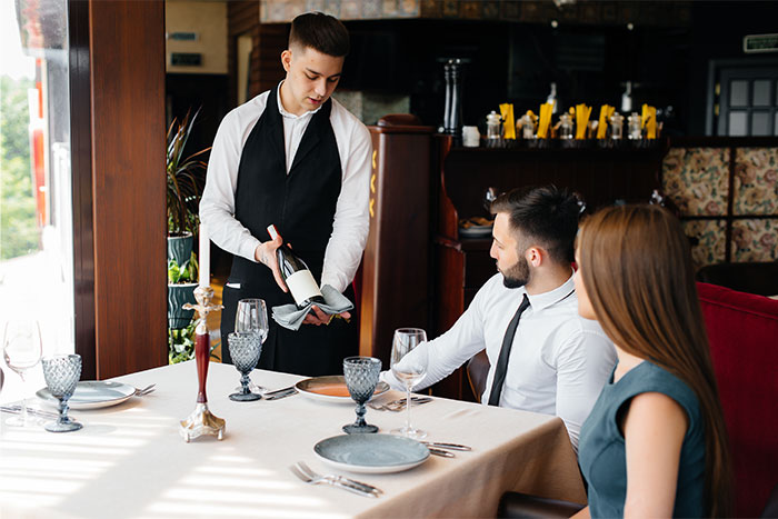 Waiter serving wine to a couple at a restaurant, illustrating servers sharing the worst dates they witnessed at work.