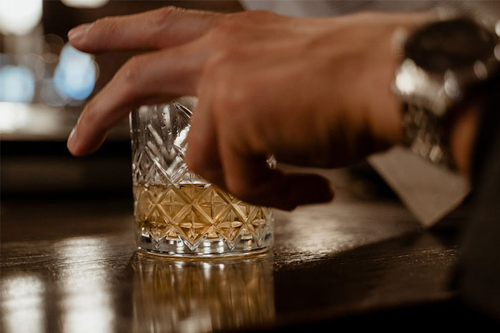 Close-up of a hand holding a glass of whiskey on a bar, illustrating servers witnessing the worst dates at work.