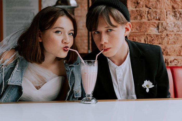 Young couple sharing a milkshake with two straws at a diner, illustrating servers witnessing the worst dates at work.