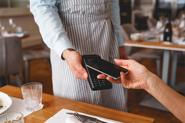 Server in striped apron accepting contactless payment from customer at restaurant table, illustrating worst dates witnessed at work