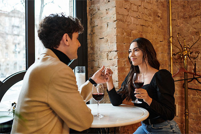 Couple on a date in a cozy restaurant, holding hands and drinking wine as servers observe worst dates at work.
