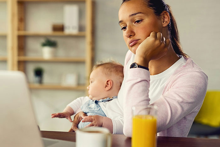 Woman sitting at a laptop looking frustrated while holding a baby, illustrating mansplain situations and eye-rolling reactions.