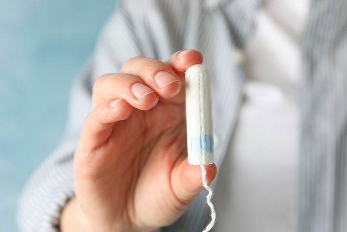 Close-up of a person holding a tampon, illustrating mansplain attempts and women’s eye-rolling reactions.