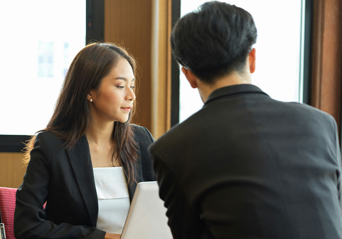 Woman rolling her eyes while man in suit tries to mansplain something during a business conversation by the window.
