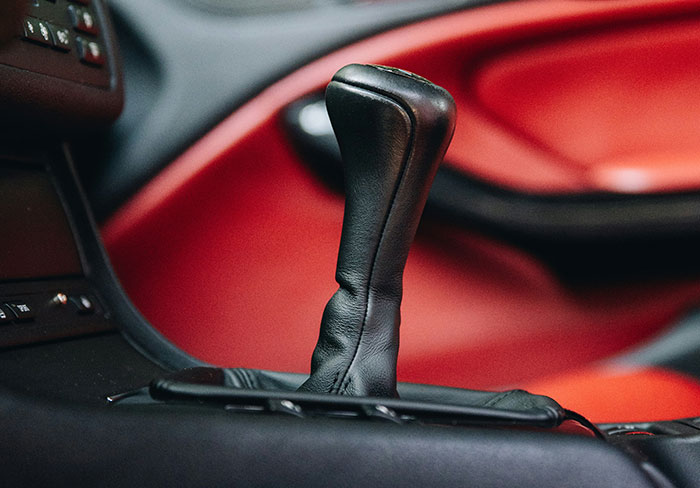 Close-up of a car's black leather gear shift k**b with red interior accents in the background.