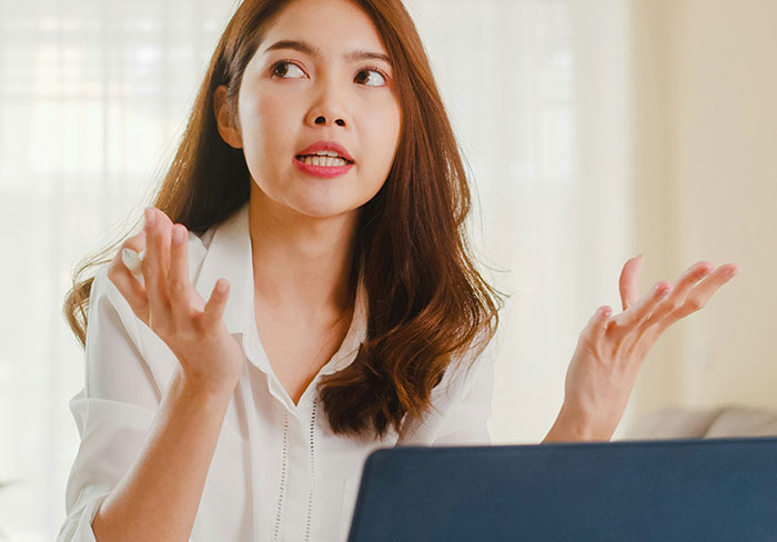 Young woman showing frustration and rolling her eyes, reacting to mansplain in a casual indoor setting with a laptop.
