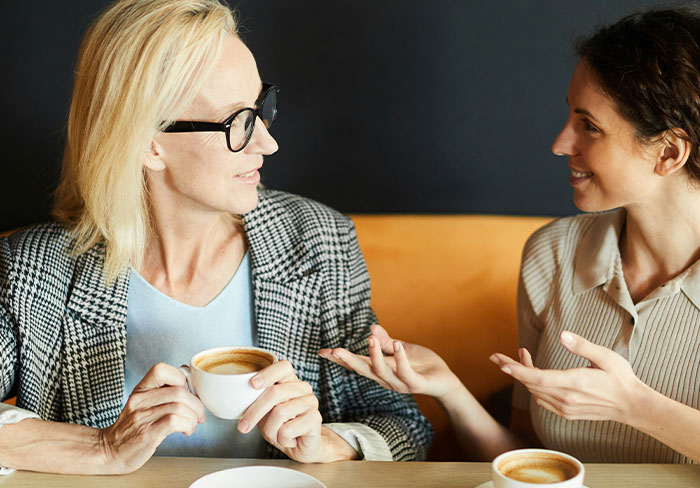 Two women having coffee and a conversation, capturing moments of mansplaining and eye-rolling reactions.