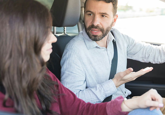 Man explaining something to a woman in a car, illustrating a mansplain moment while she looks unimpressed and rolls her eyes.