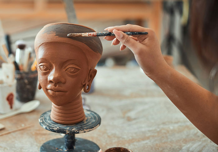 Artist painting a detailed clay sculpture head, symbolizing creativity while guys mansplain and women roll their eyes.