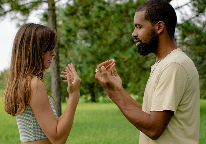 Man and woman outdoors, man gesturing while woman rolls her eyes, illustrating mansplain and reaction dynamics.