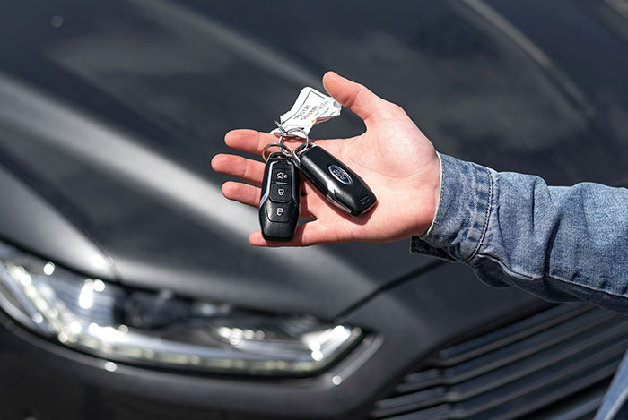 Hand holding car keys in front of a black vehicle, illustrating mansplain moments with women rolling their eyes.