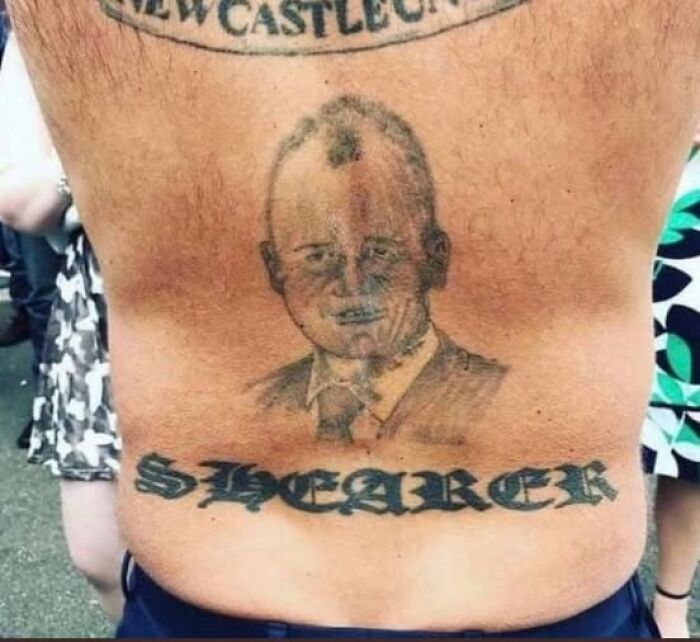 Tattoo of a poorly drawn man's portrait with the word SPEAKER inked below, shown on a person's lower back among other tattoos.
