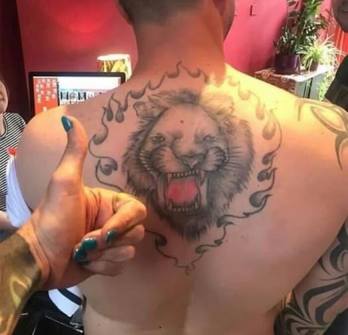 Tattoo of a roaring lion with flames on a man's back, featured among abysmally bad tattoos on dedicated Facebook pages.