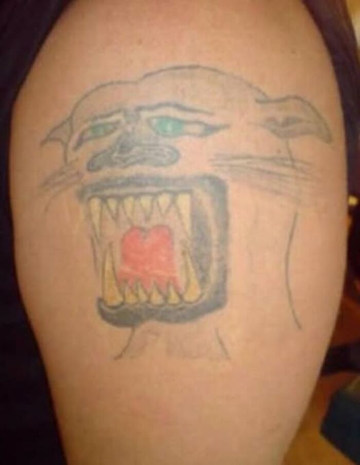 Tattoo of a poorly drawn fierce animal face with open mouth and sharp teeth on a person's arm, showcasing bad tattoos.