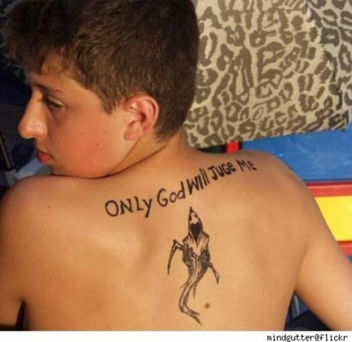 Young man showing abysmally bad tattoo on back with text and grim reaper design, highlighting worst tattoo examples.