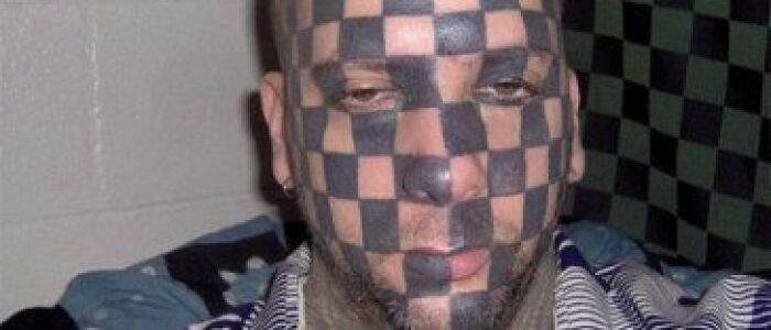 Man with abysmally bad tattoos of a black and skin-tone checkerboard pattern covering his entire face and head