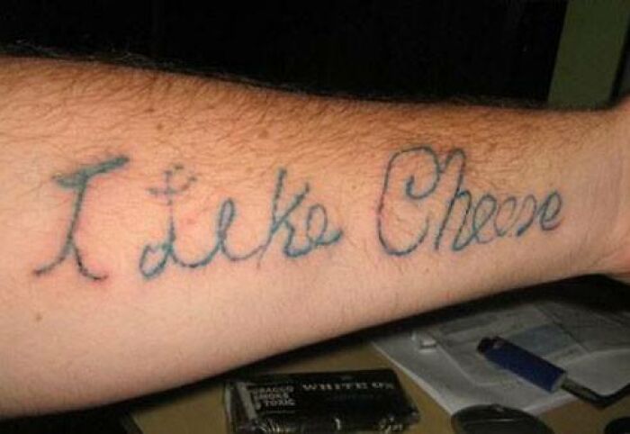 Arm tattoo with poorly done cursive text spelling I Like Cheese, showcasing one of the worst bad tattoos in the collection.