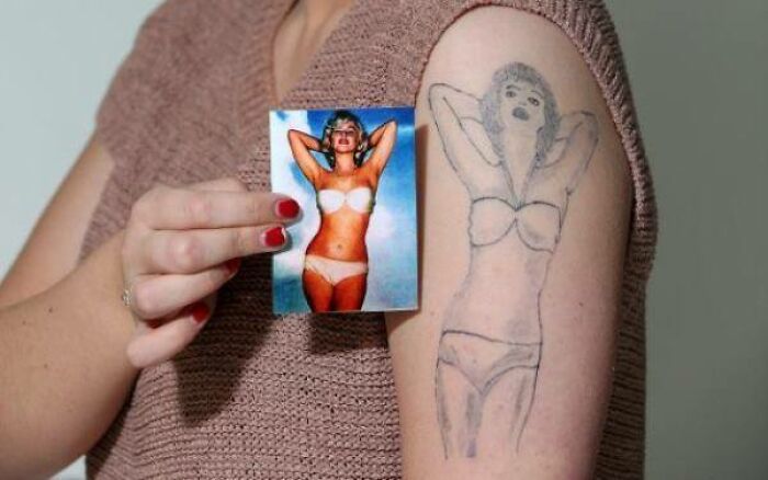 Hand holding a photo of a woman in a bikini next to an abysmally bad tattoo of the same image on their upper arm.
