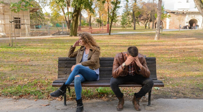 A young man and woman sitting apart on a bench in a park, showing conflict in a would you rather poll scenario.