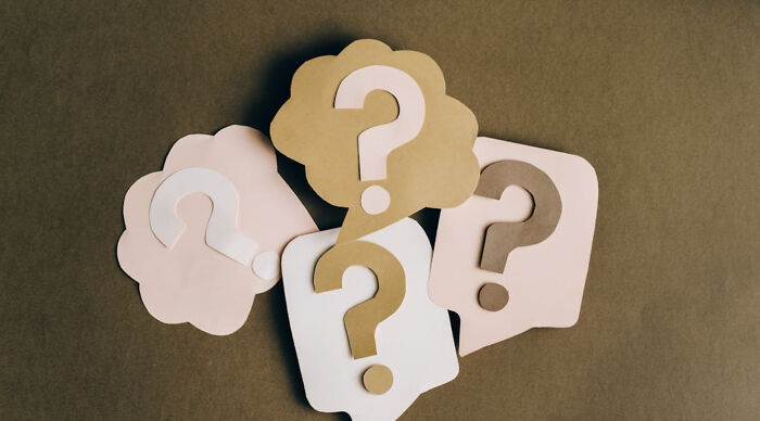 Paper cutout question marks in speech bubbles on a brown surface representing a Would You Rather poll concept.
