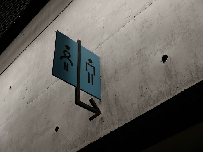 Bathroom signs with an arrow on a concrete wall highlighting surprising things travelers share about the U.S. visit experiences